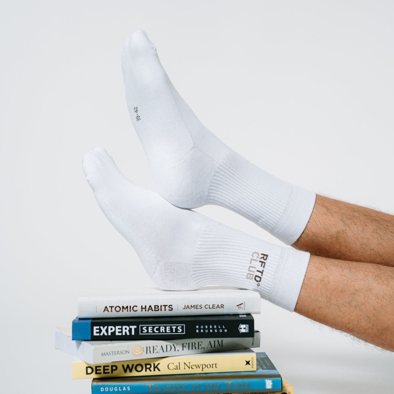 Beine werden auf einem Stapel von Büchern abgelegt und zu sehen sind die Beine und an den Füßen sind die RFTD Sportsocken.