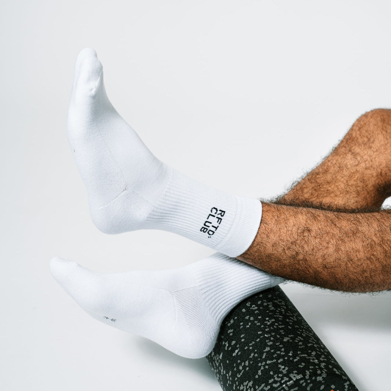 Zu sehen sind die Füße eines Mannes der Sportsocken trägt und diese auf einer Blackroll abstützt